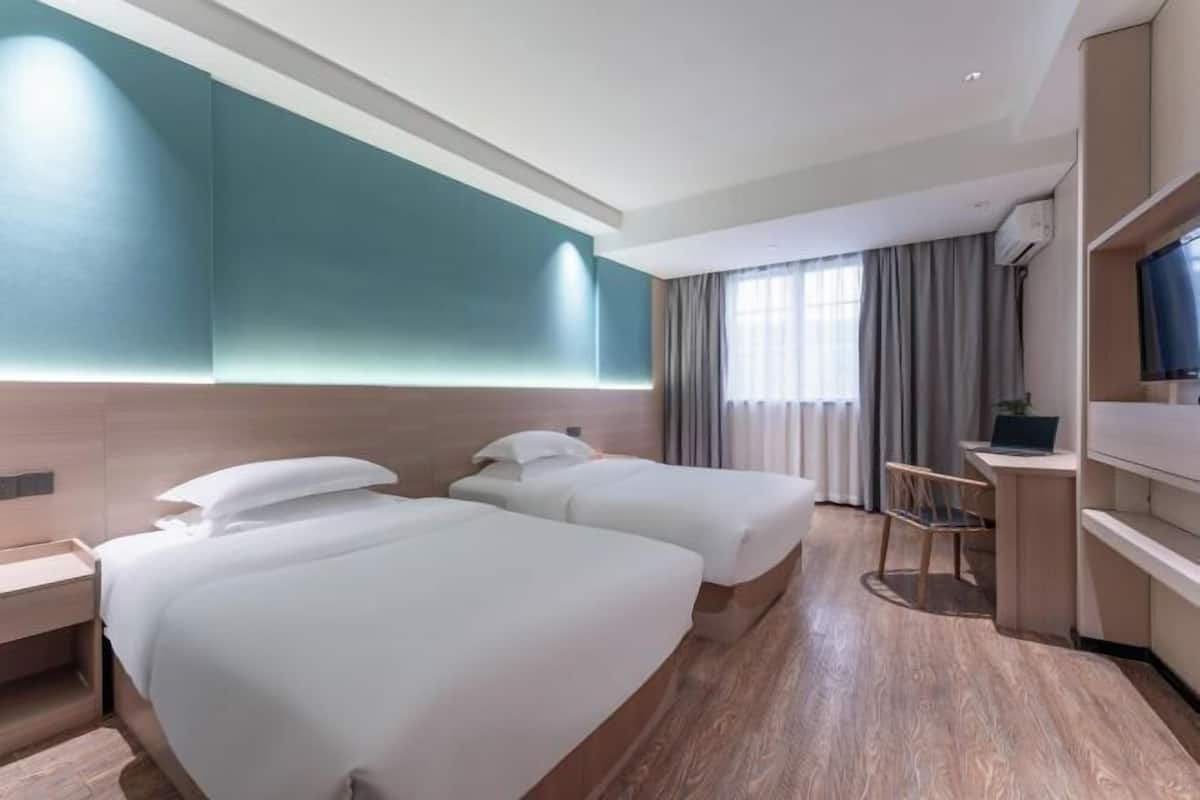A hotel room with two beds, a desk, a chair, a TV, and a window with curtains.