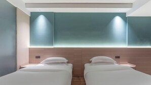 Habitación de hotel con dos camas individuales, suelo de madera y una pared de acento color aguamarina con iluminación empotrada.