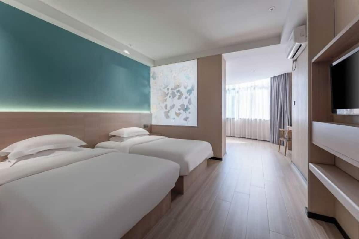 A hotel room with two beds, a television, and a large window with curtains.