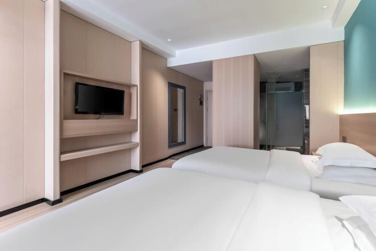 A modern hotel room with a large bed, a flat-screen TV mounted on the wall, and a walk-in shower.