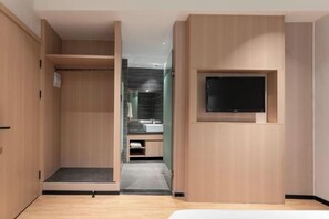 Une chambre à coucher comprenant un lit, un téléviseur fixé au mur, un dressing et une salle de bain avec un lavabo et un miroir.