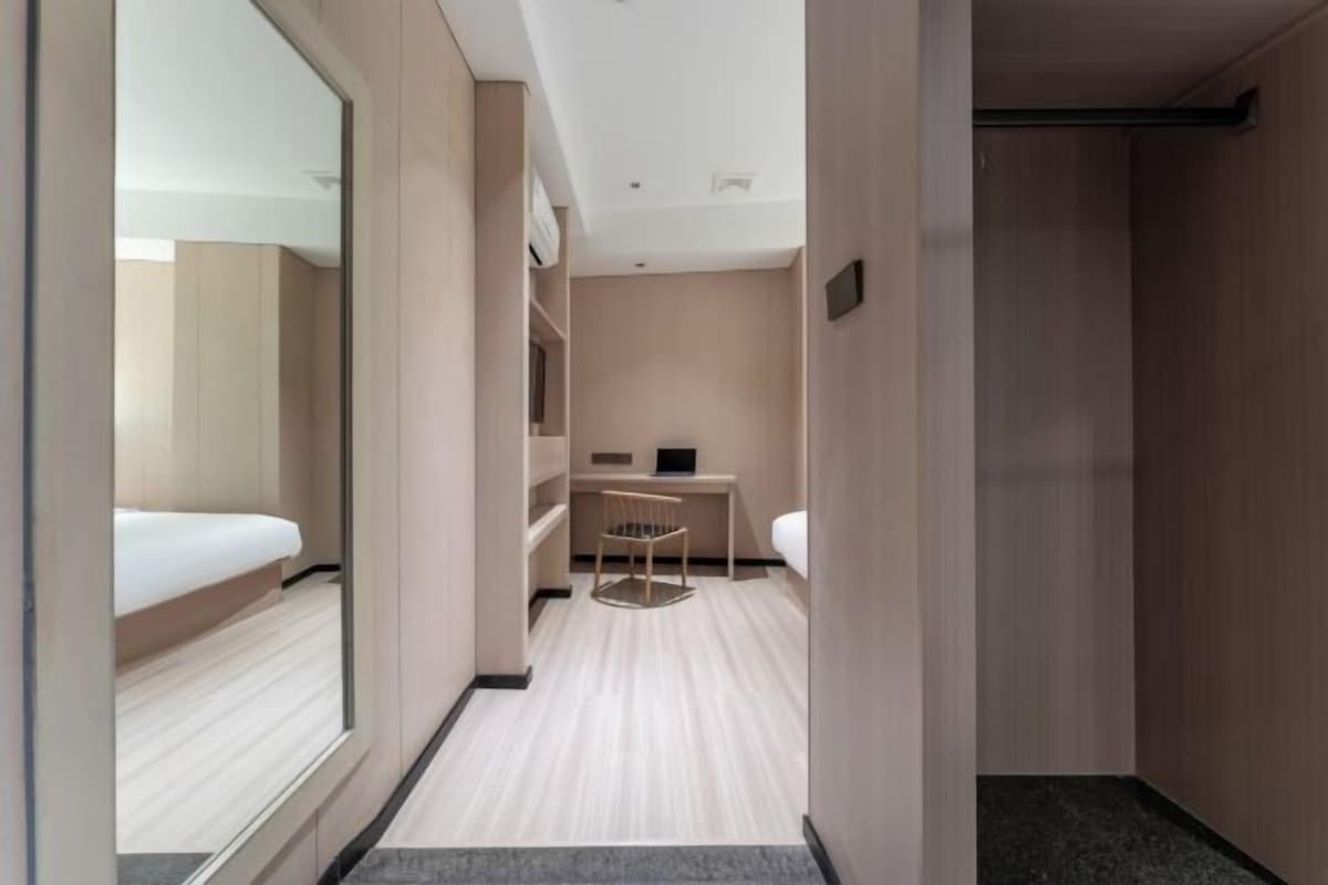 A modern hotel room with a large mirror, a bed, a desk with a chair, and a small seating area.