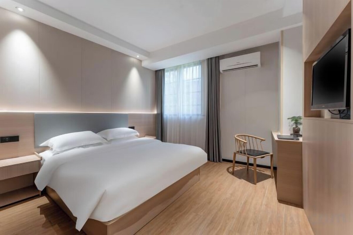 A modern hotel room with a large bed, a desk, a chair, and a TV.
