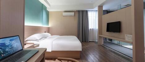 A modern hotel room with a bed, a desk with a laptop, a TV on a stand, and a window with curtains.