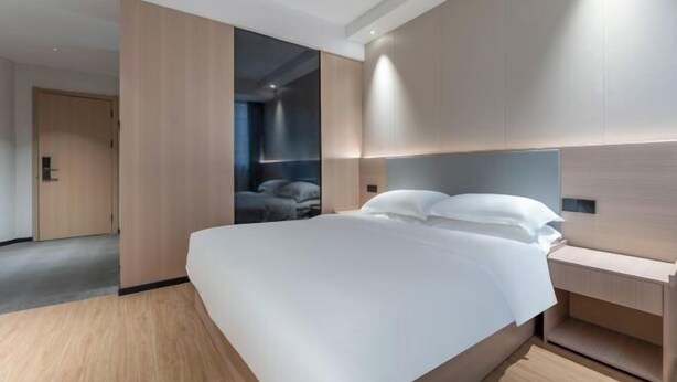 Una habitación de hotel moderna con una cama grande, una mesita de noche, un armario y vistas a otra habitación.