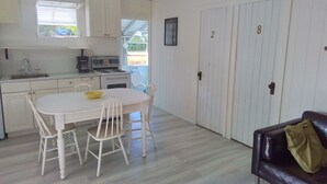 A compact kitchen with white cabinets, a dining table with chairs, a stove, and a sink. There are two doors with numbers 2 and 8 on them.