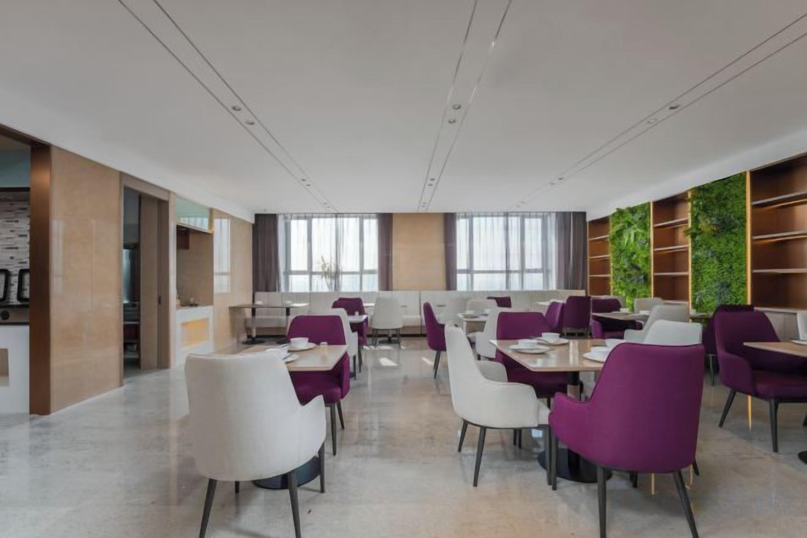 A modern dining area with tables and chairs, large windows, and a green wall with plants.