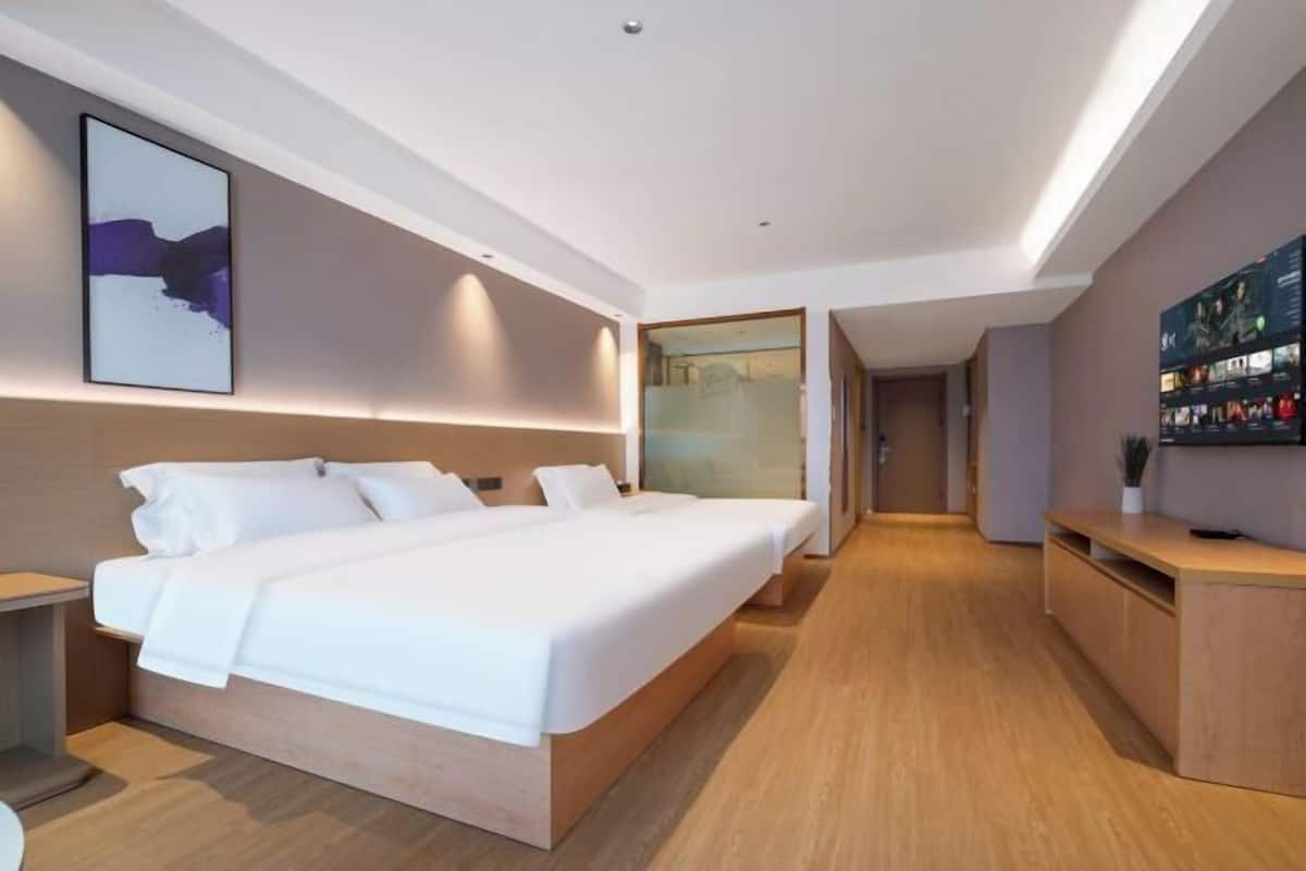 A modern hotel room with a large bed, bedside tables, a TV, and a painting on the wall.