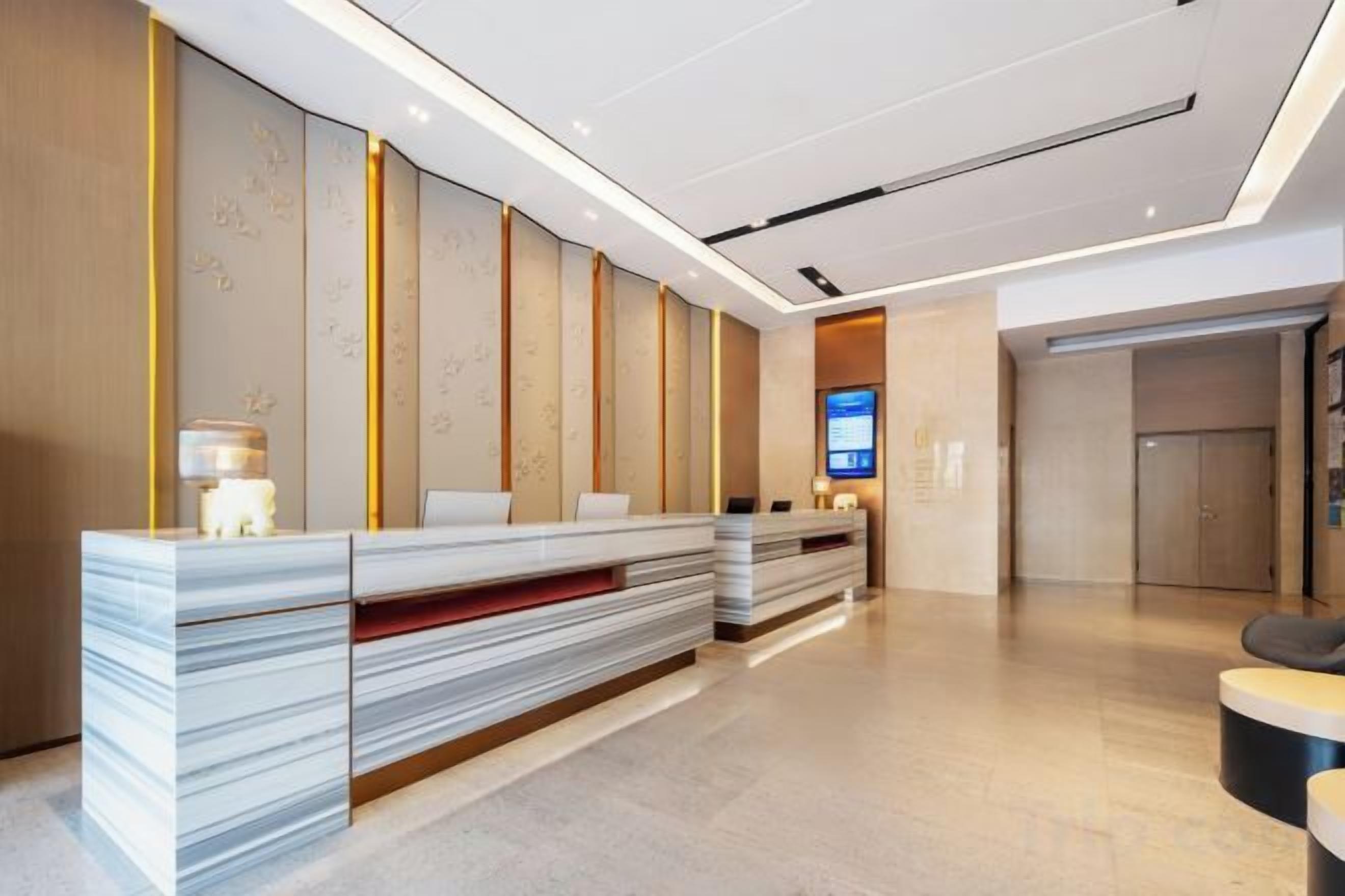 Zona de recepción de hotel con diseño moderno, que incluye un mostrador de recepción, un área de descanso y una pantalla digital.