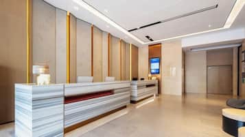 A hotel reception area with a modern design, featuring a reception desk, seating area, and a digital screen.