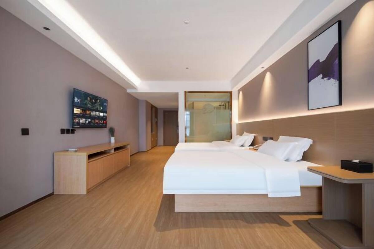 A modern hotel room with a large bed, a TV mounted on the wall, and a wooden floor.