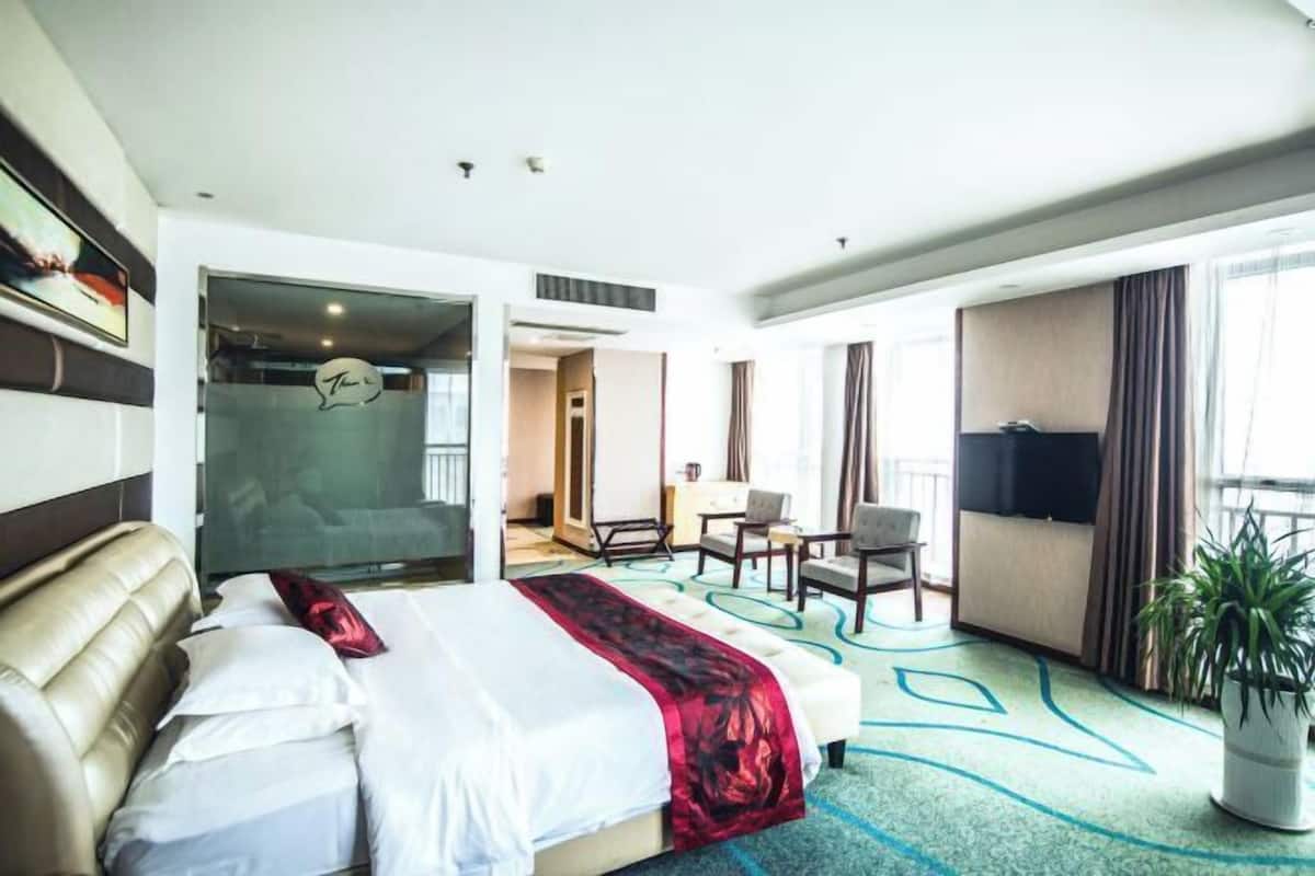 A hotel room with a bed, a desk, a chair, a TV, and a potted plant.