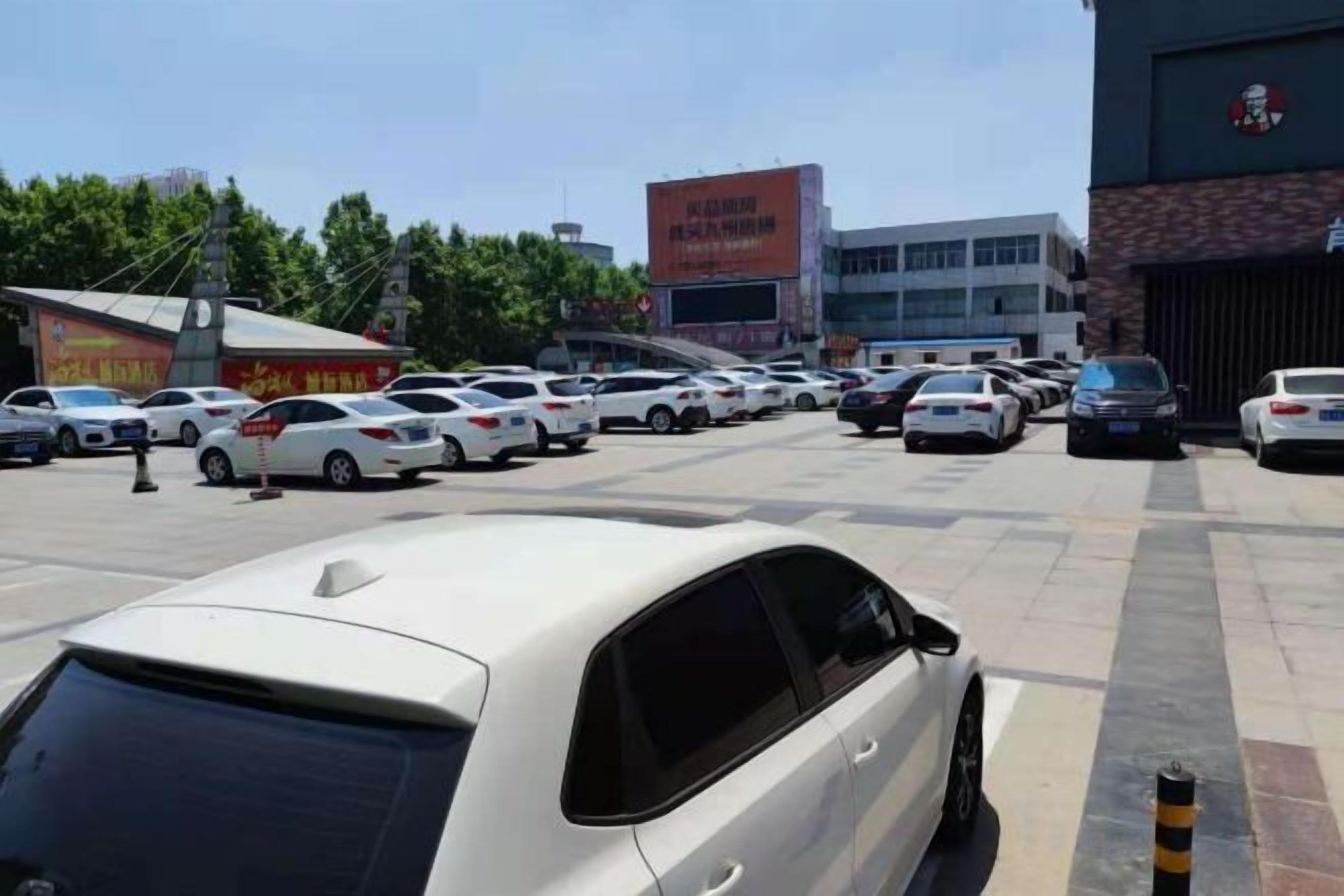 A parking lot with multiple cars, a building with a sign, and trees in the background.