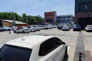 A parking lot with multiple cars, a building with a sign, and trees in the background. - Thank You Intercity Hotel (Junan Leshang Building) (Junan County)