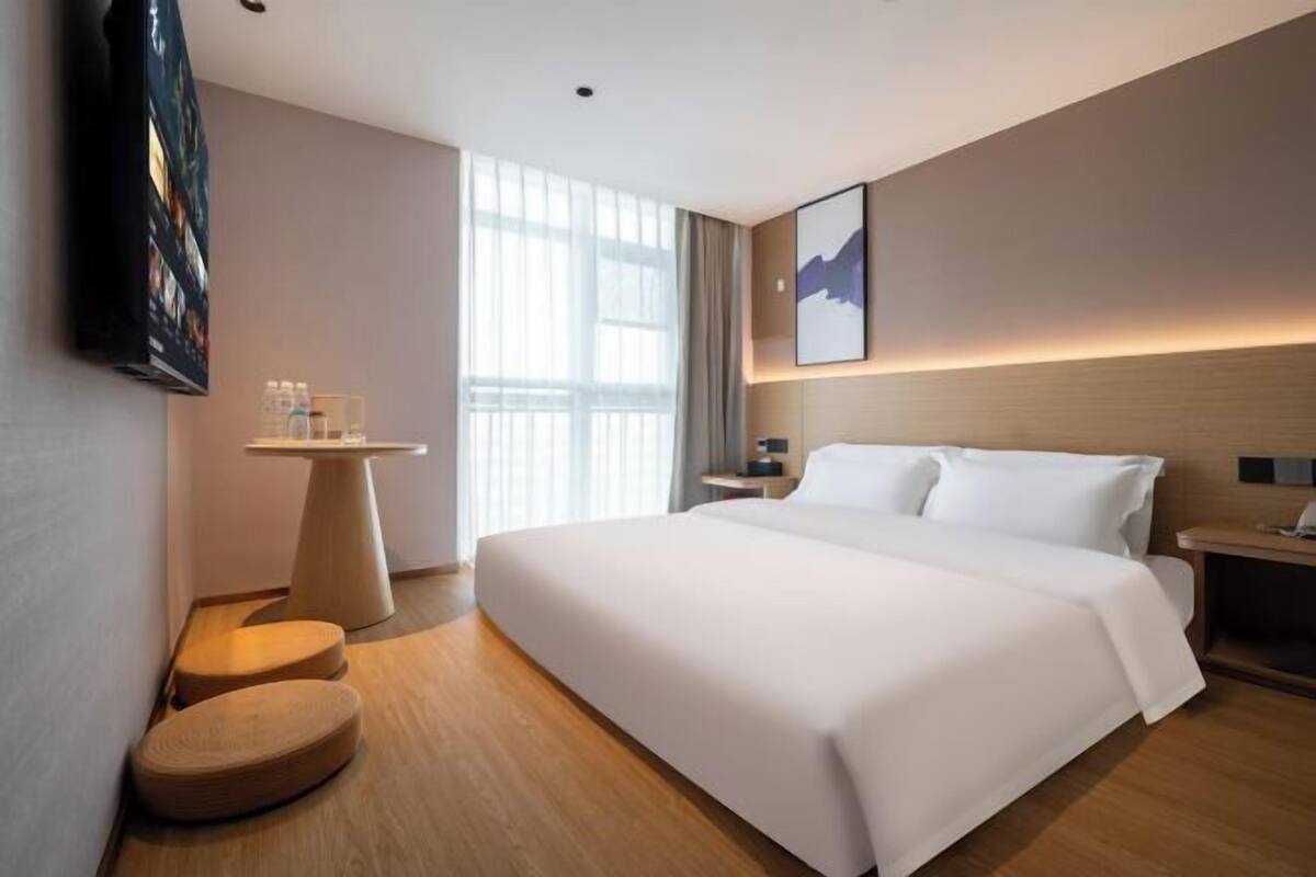 A hotel room with a large bed, a small table, a TV, and a window with curtains.