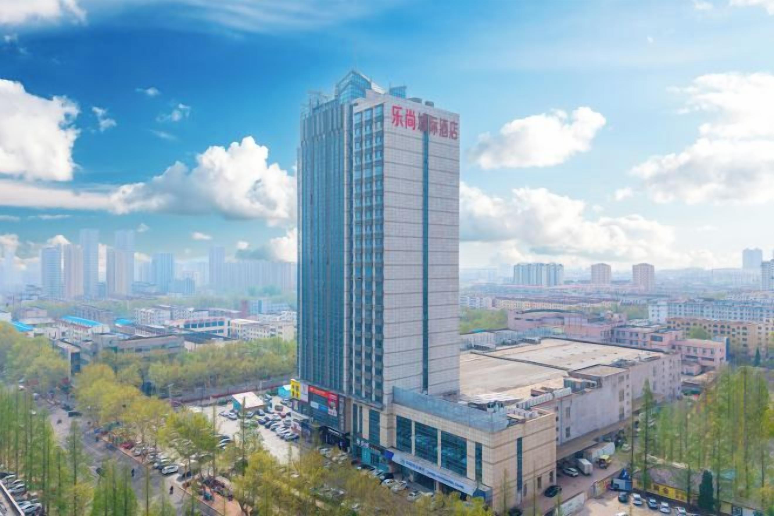 A tall hotel with a modern design, surrounded by a cityscape and greenery.