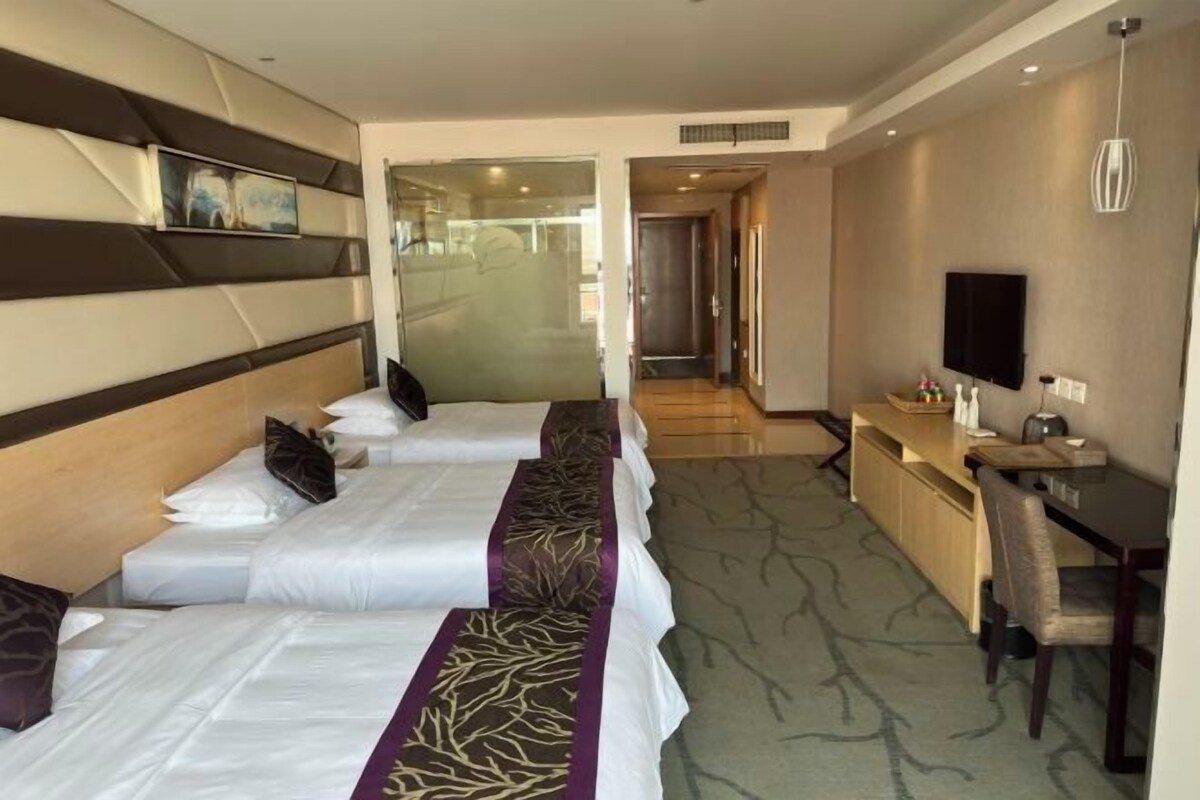 Une chambre d’hôtel avec deux lits, un bureau, une chaise, une télévision et une fenêtre.