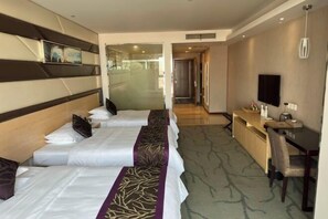 A hotel room with two beds, a desk, a chair, a television, and a window.