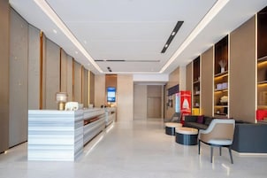 Un vestíbulo de hotel con mostrador de recepción, zona de estar y pantalla digital.