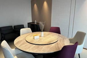 Una mesa redonda con tapa de mármol rodeada de sillas, un florero con plantas secas y una caja blanca pequeña.