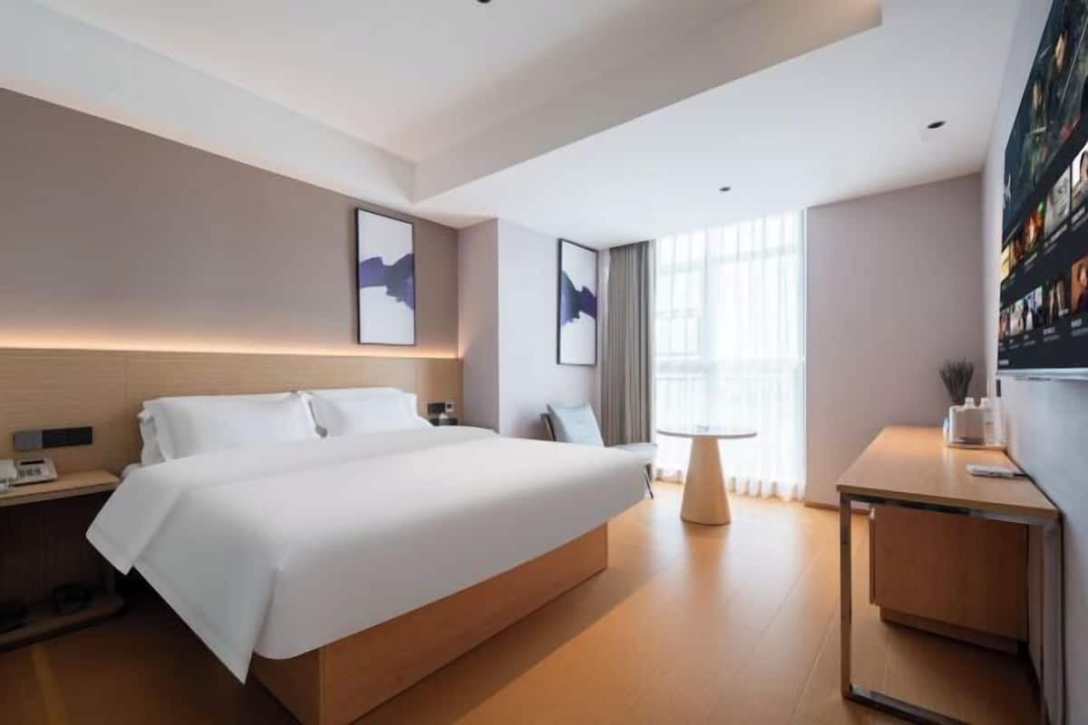 A modern hotel room with a large bed, bedside tables, a desk, and artwork on the walls.