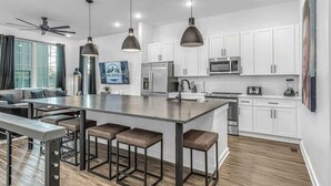 A modern kitchen with white cabinets, stainless steel appliances, and a central island with bar stools. - Johnny Cash House • Walk to Bars & Dining (Nashville)