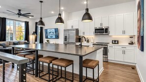 A modern kitchen with white cabinets, a central island with stools, and a ceiling fan.