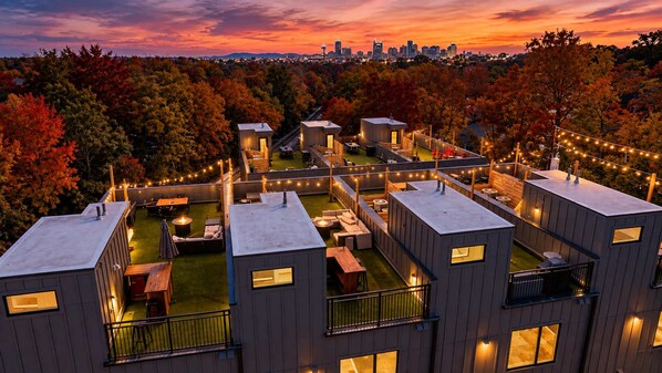 A modern residential complex with multiple units, outdoor seating areas, and a view of a city skyline at dusk.
