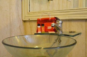 A glass bowl sink with a faucet and a mirror above it. There are toiletries on a shelf next to the sink. - OYO Rooms Nehru Enclave (New Delhi)