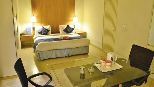 Una habitación de hotel con una cama, mesitas de noche con lámparas, una mesa de centro de vidrio con una bandeja de tazas y una silla.