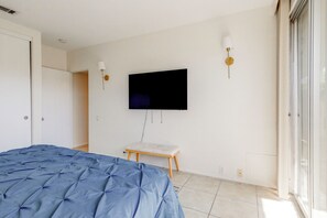 Un dormitorio con una cama, un televisor montado en la pared y una mesita.