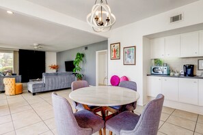 A modern living room with a dining table, sofas, and a kitchen area with cabinets and appliances.