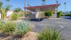 Un espace de stationnement doté d’une structure abritée, de palmiers et de plantes désertiques.