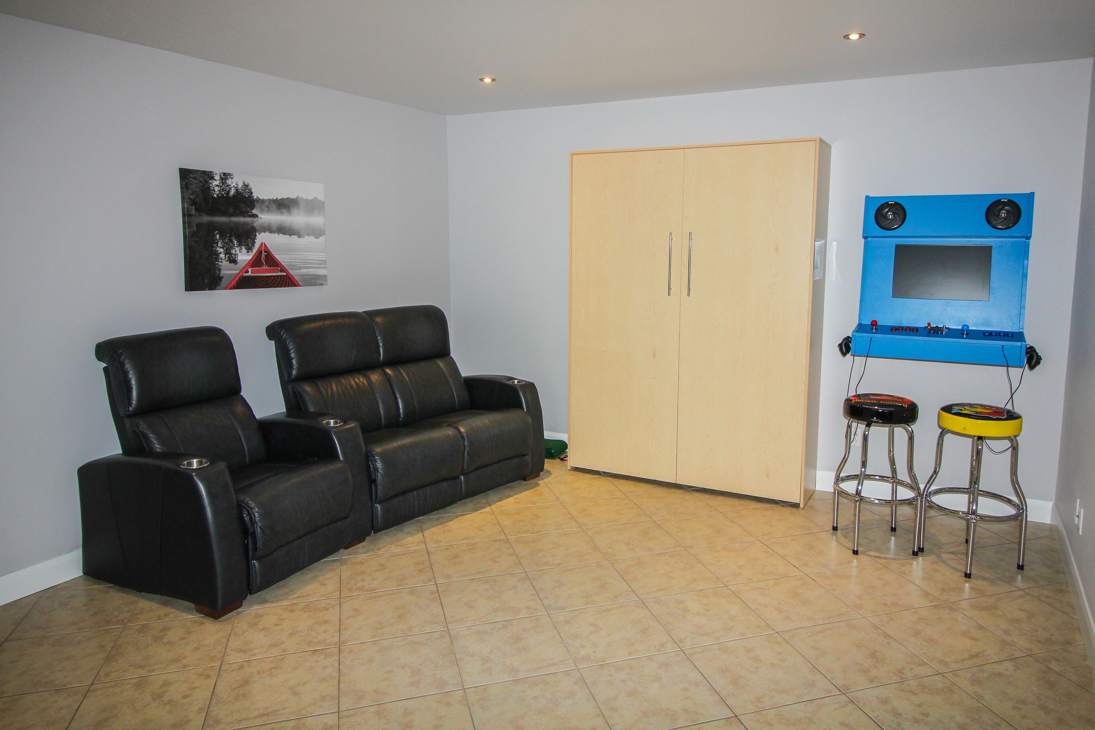A living room with a black leather sofa, a wooden wardrobe, and a blue entertainment unit with two speakers.