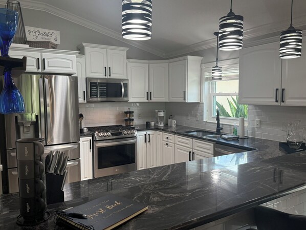 A modern kitchen with white cabinets, stainless steel appliances, and a marble countertop.