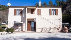 A two-story building with a stone facade, a covered patio with chairs, and a small table. - A03 - Massignano, two room apartment (Ancona)