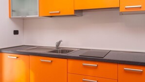A kitchen with orange cabinets, a black countertop, and a stainless steel sink. - A03 - Massignano, two room apartment (Ancona)