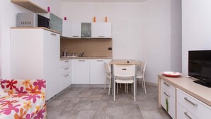 Een kleine keuken met witte kastjes, een magnetron, een spoelbak en een eethoek met een tafel en stoelen.