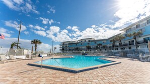 En swimmingpool med ett kaklat poolområde, en flagga och en byggnad med balkonger i bakgrunden.