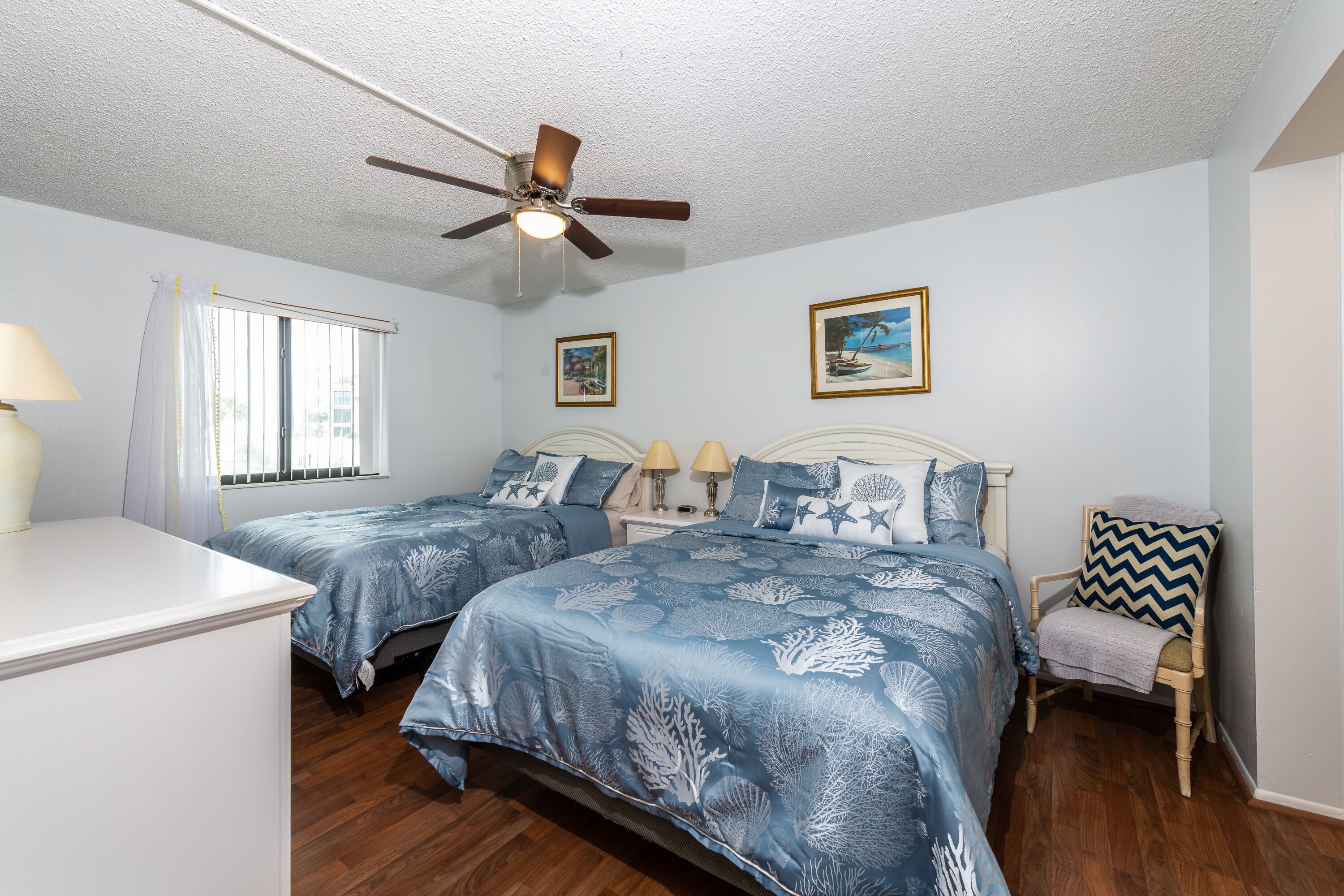 A bedroom with two beds, a ceiling fan, a chair, and a window with curtains.