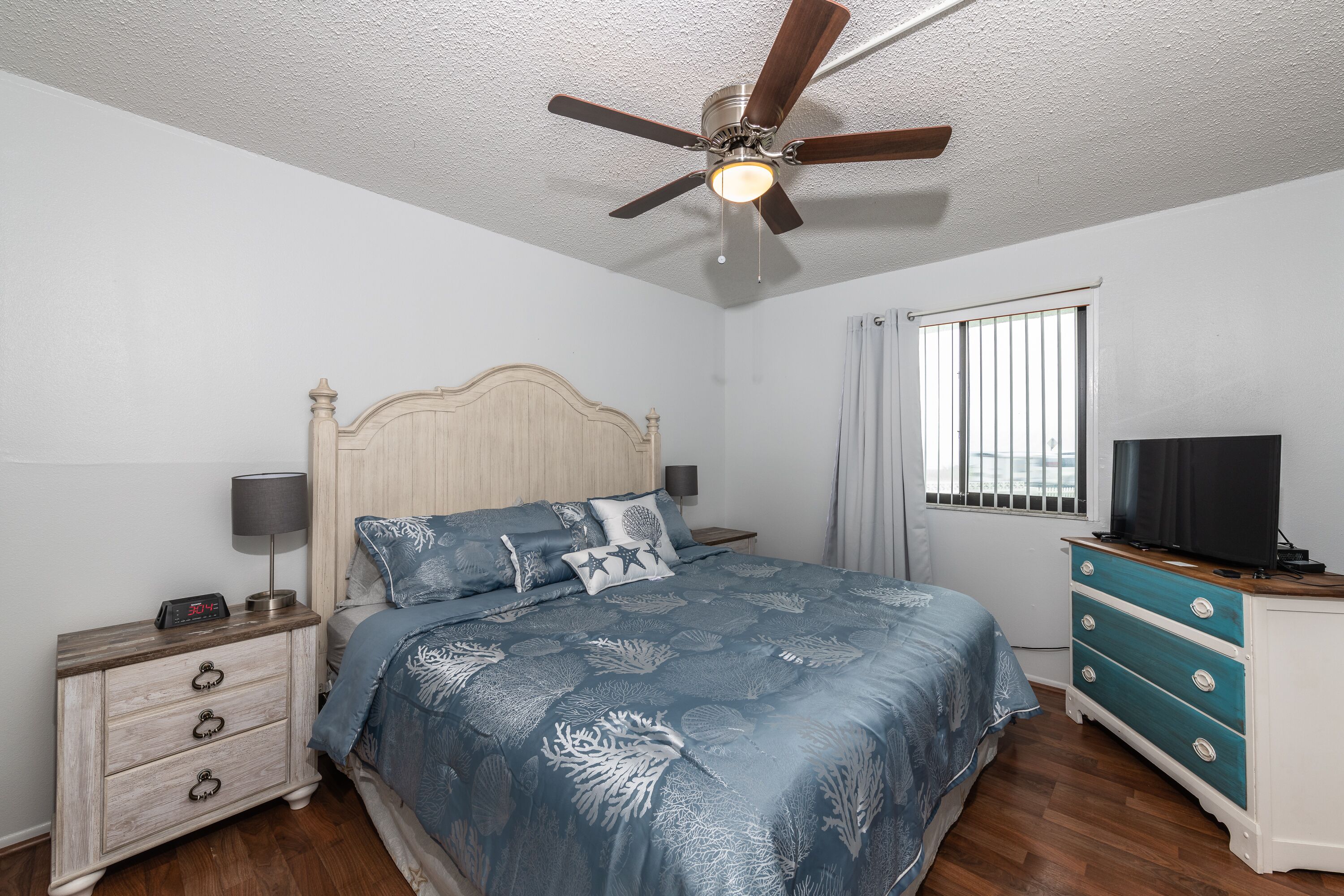 A bedroom with a bed, nightstand, dresser, ceiling fan, and window.