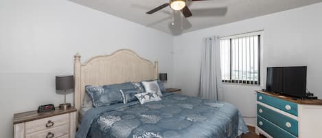 A bedroom with a bed, nightstand, dresser, ceiling fan, and window.