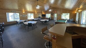A lodge with wooden walls, a pool table, and multiple dining tables.