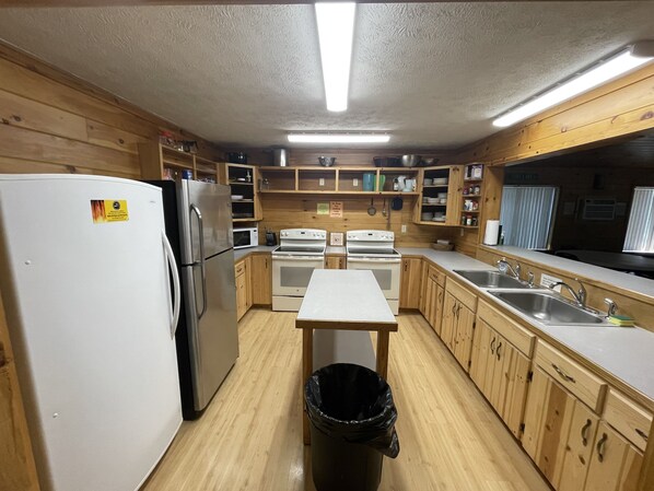 A compact kitchen with wooden cabinets, a refrigerator, a microwave, an oven, and a sink. - Vacation Lodge for Big Groups: 8BR/8BTH, Sleeps 36, Pool Table, Vball, Fire Pit (Indian River)