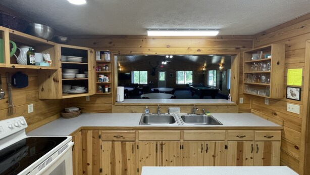A wooden cabin-style kitchen with a stove, sink, and dining area visible through a large window.