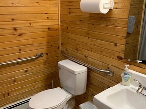 A small, wooden-paneled bathroom with a toilet, a handrail, a sink, and a soap dispenser. - Vacation Lodge for Big Groups: 8BR/8BTH, Sleeps 36, Pool Table, Vball, Fire Pit (Indian River)