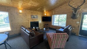 A cozy cabin interior with a fireplace, leather sofas, plaid ottoman, and a mounted deer head.