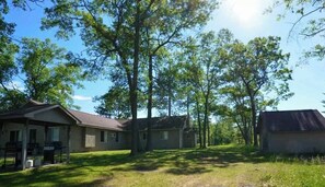 A residential area with two houses, one with a porch and grill, surrounded by trees. - Vacation Lodge for Big Groups: 8BR/8BTH, Sleeps 36, Pool Table, Vball, Fire Pit (Indian River)