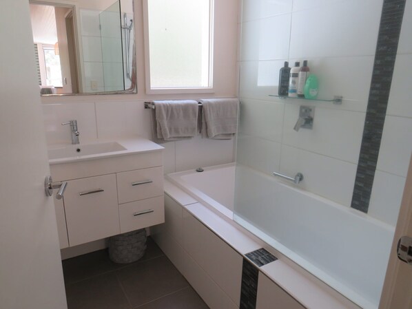 Une salle de bain moderne avec une baignoire, un lavabo, un miroir et une fenêtre.