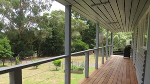 A covered wooden deck with a metal railing, overlooking a grassy area with trees.
